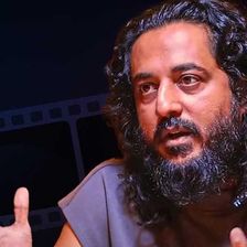 Sajid Yahiya with long hair and a beard, mid-conversation portrait