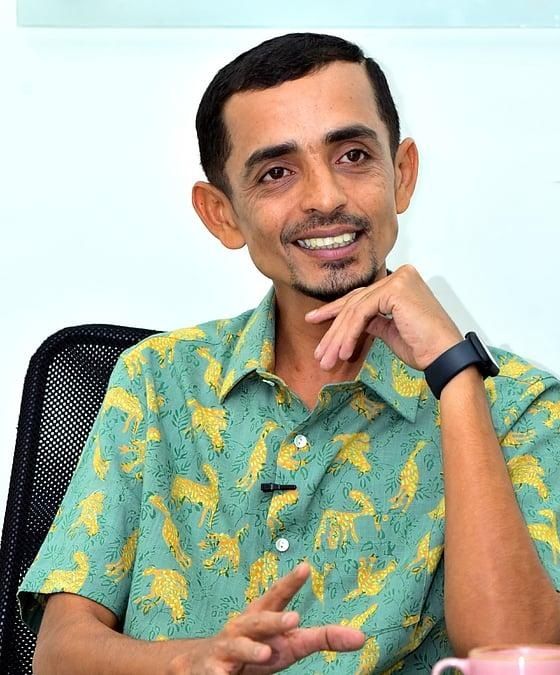 Rajesh Madhavan smiling in a printed green shirt, seated portrait