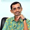 Rajesh Madhavan smiling in a printed green shirt, seated portrait