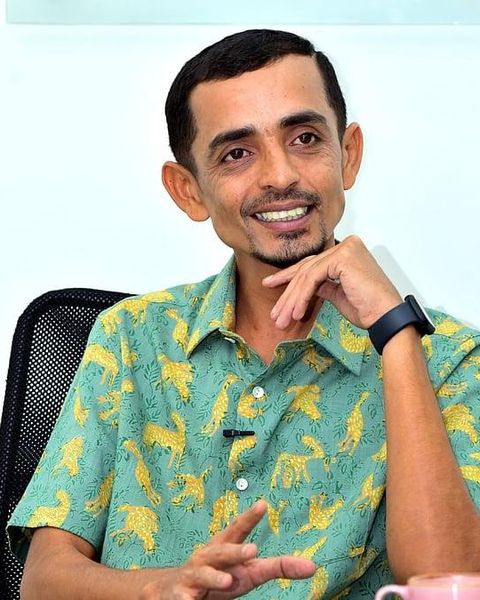 Rajesh Madhavan smiling in a printed green shirt, seated portrait