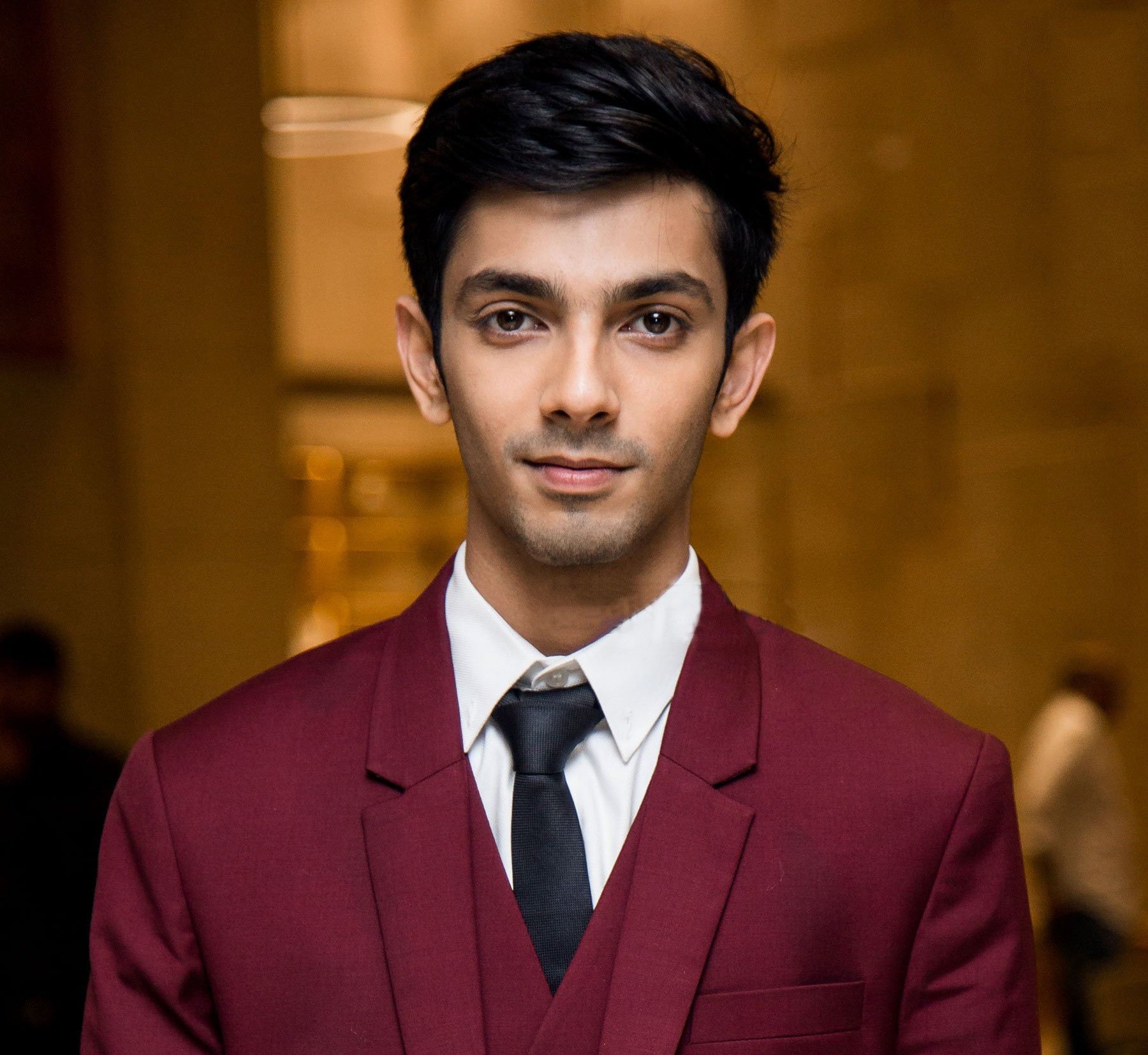 Anirudh Ravichander in a maroon suit and black tie, formal portrait