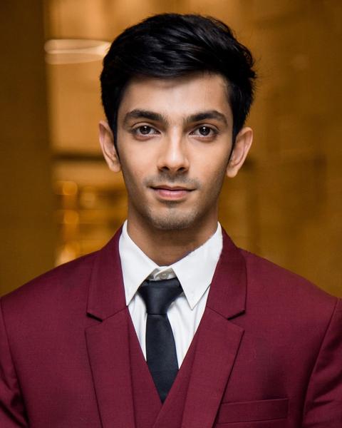 Anirudh Ravichander in a maroon suit and black tie, formal portrait