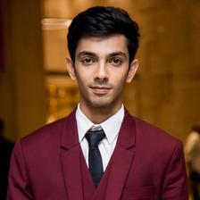 Anirudh Ravichander in a maroon suit and black tie, formal portrait