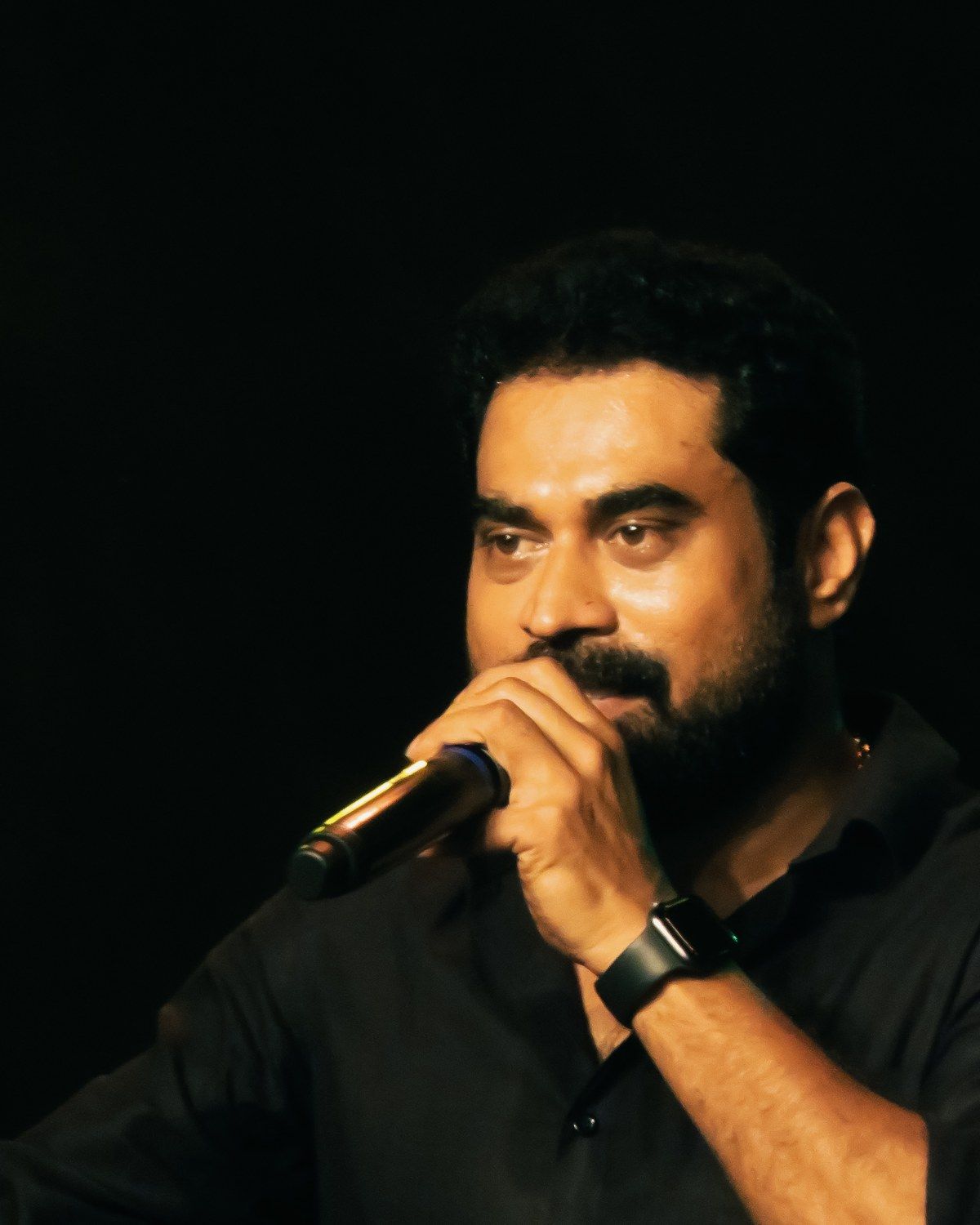 Suraj Venjaramoodu speaking into a microphone on a dark stage