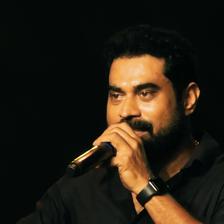 Suraj Venjaramoodu speaking into a microphone on a dark stage