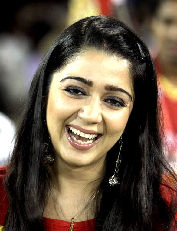 Charmme Kaur laughing in a red and yellow jersey at a stadium