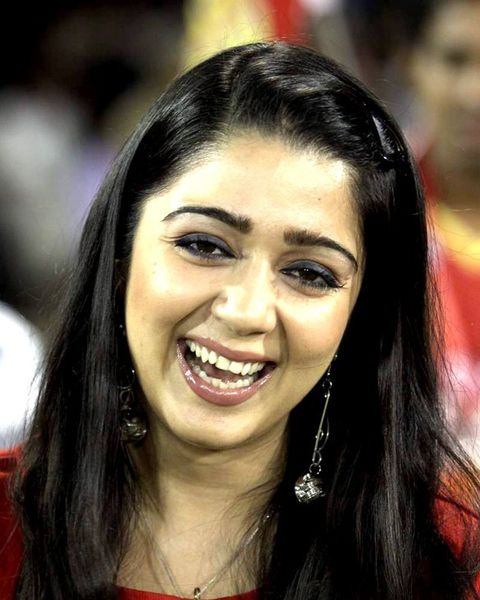 Charmme Kaur laughing in a red and yellow jersey at a stadium