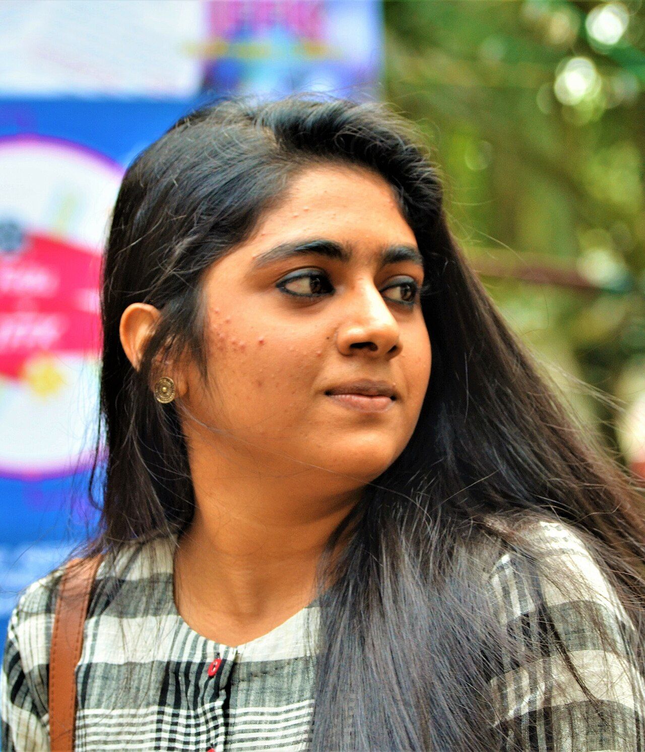 Nimisha Sajayan in a checked shirt glancing to the side outdoors