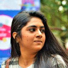 Nimisha Sajayan in a checked shirt glancing to the side outdoors