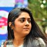 Nimisha Sajayan in a checked shirt glancing to the side outdoors