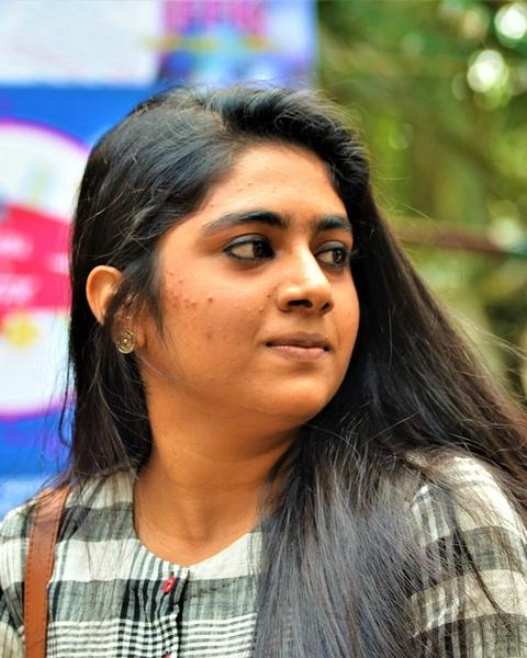 Nimisha Sajayan in a checked shirt glancing to the side outdoors