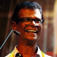 Indrans laughing in glasses beside a microphone at an event