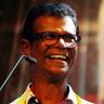 Indrans laughing in glasses beside a microphone at an event