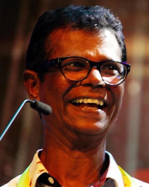 Indrans laughing in glasses beside a microphone at an event