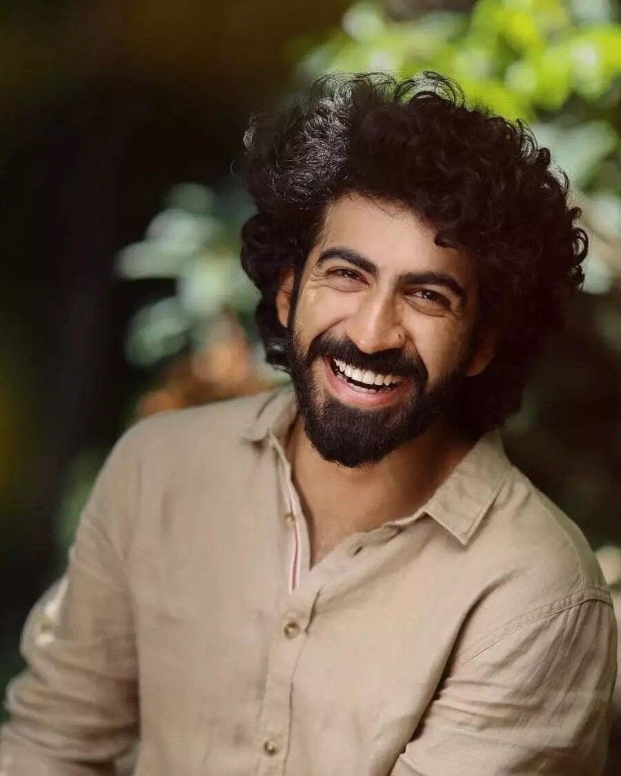 Roshan Mathew smiling with curly hair and a beard outdoors