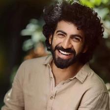 Roshan Mathew smiling with curly hair and a beard outdoors