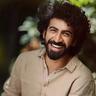 Roshan Mathew smiling with curly hair and a beard outdoors