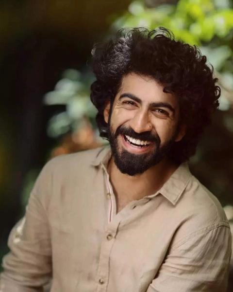 Roshan Mathew smiling with curly hair and a beard outdoors