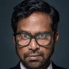 Guru Somasundaram in glasses, suit and red tie against a dark background