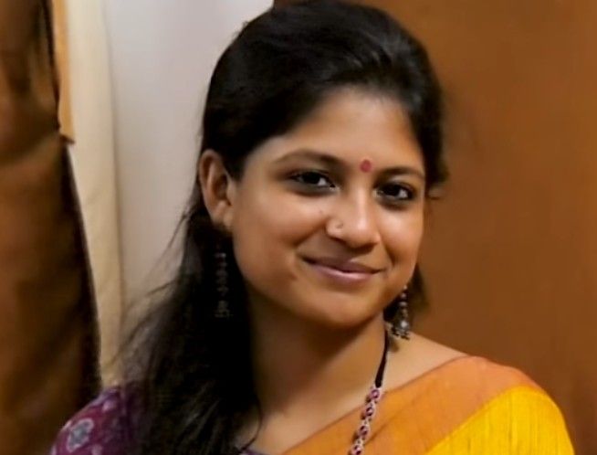 Aditi Balan smiling in a yellow and orange saree with a red bindi and dangling earrings, close-up portrait