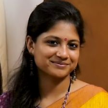 Aditi Balan smiling in a yellow and orange saree with a red bindi and dangling earrings, close-up portrait
