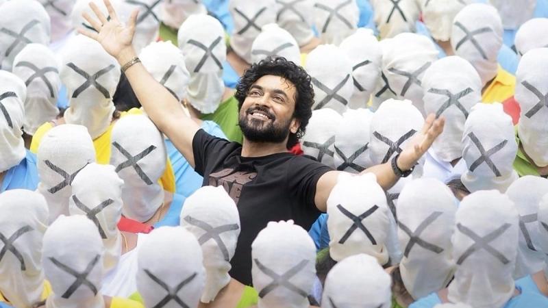 Suriya, arms raised and smiling, in a crowd of masked people in the Aeroplane song poster from Scene.