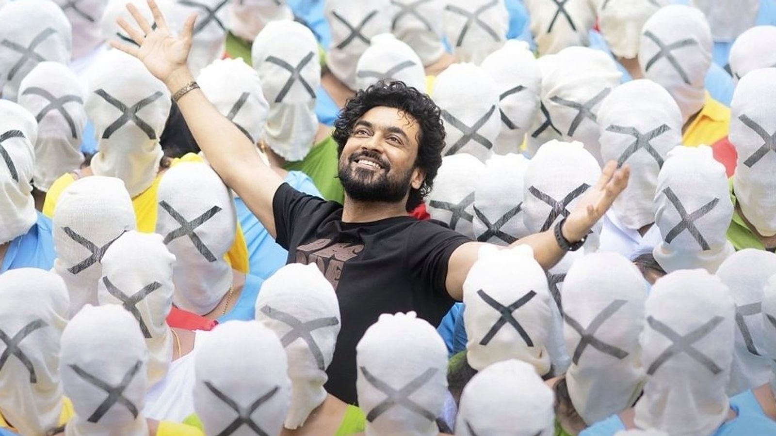 Suriya, arms raised and smiling, in a crowd of masked people in the Aeroplane song poster from Scene.