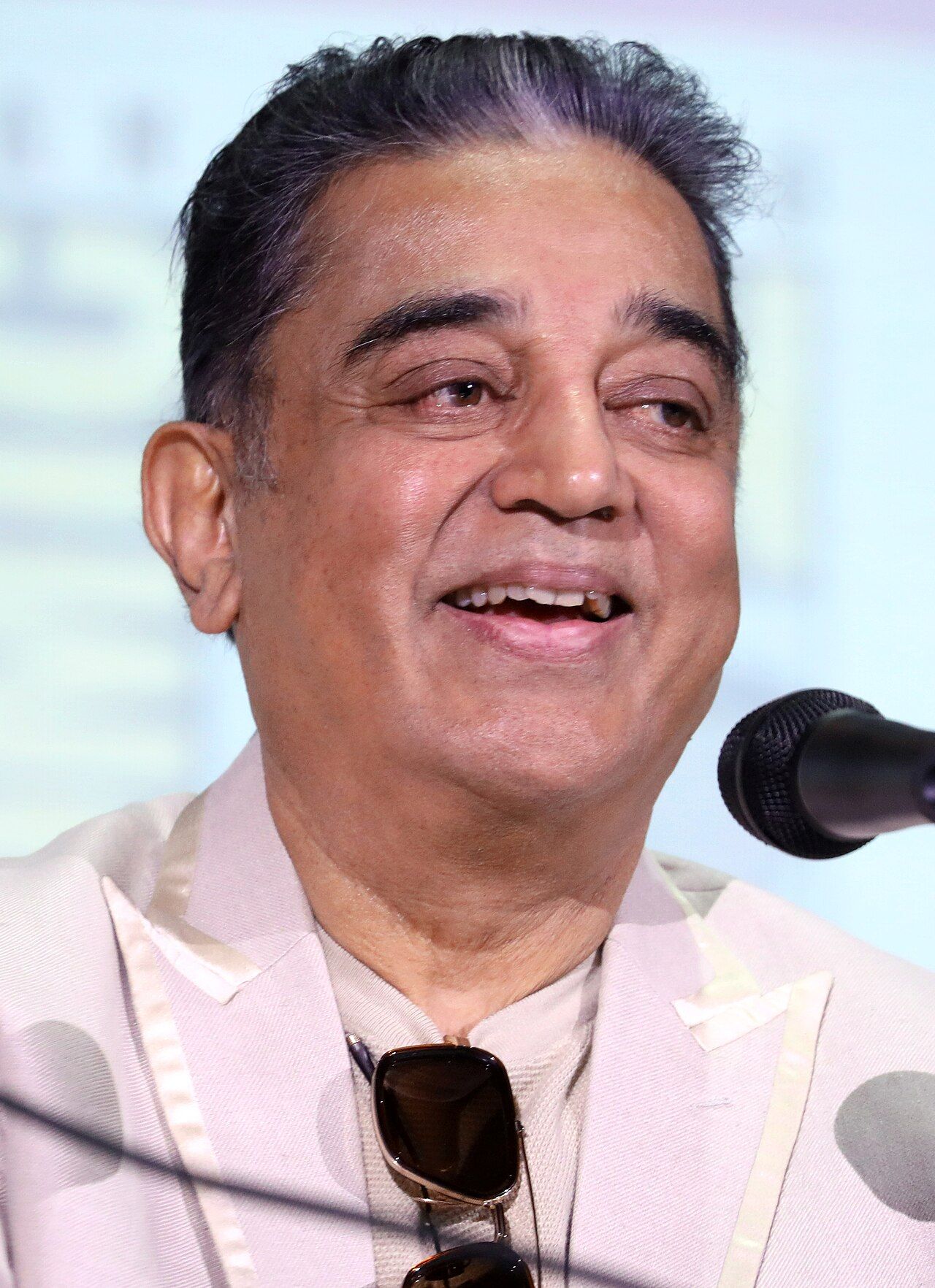 Kamal Haasan smiling at a microphone in a light jacket