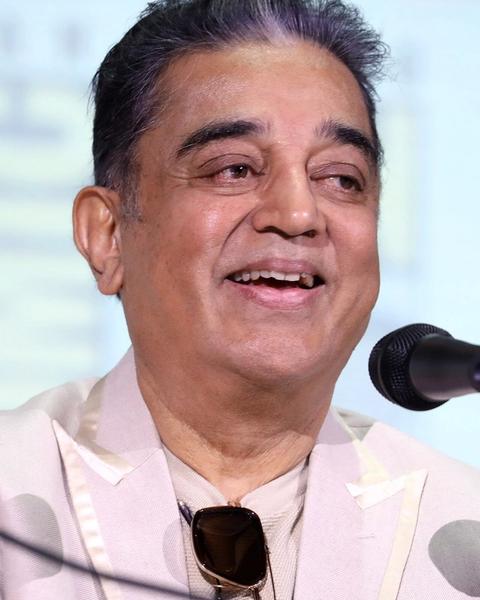 Kamal Haasan smiling at a microphone in a light jacket