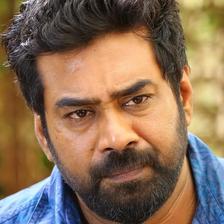 Biju Menon with a beard in a blue shirt, close-up portrait