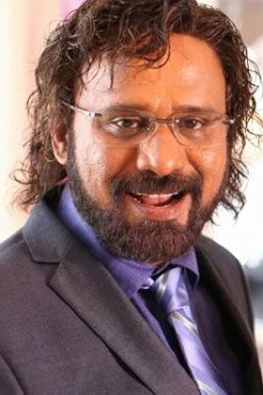 Rafi with glasses and a beard in a dark suit, smiling