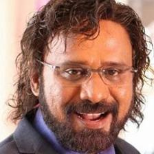 Rafi with glasses and a beard in a dark suit, smiling