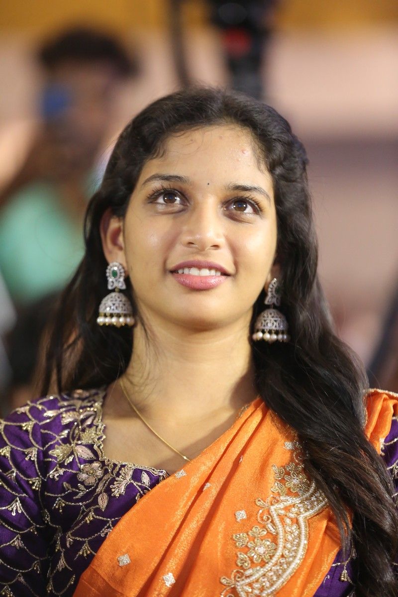 Sri Devi Apalla smiling in a purple embroidered blouse, orange saree and jhumka earrings at an event