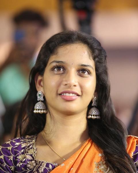 Sri Devi Apalla smiling in a purple embroidered blouse, orange saree and jhumka earrings at an event