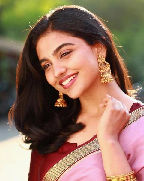 Mamitha Baiju smiling in a pink saree with gold earrings