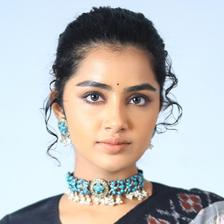 Anupama Parameswaran with her hair tied back, wearing a turquoise choker and a black-and-white ikat saree, looking at the camera against a pale blue backdrop