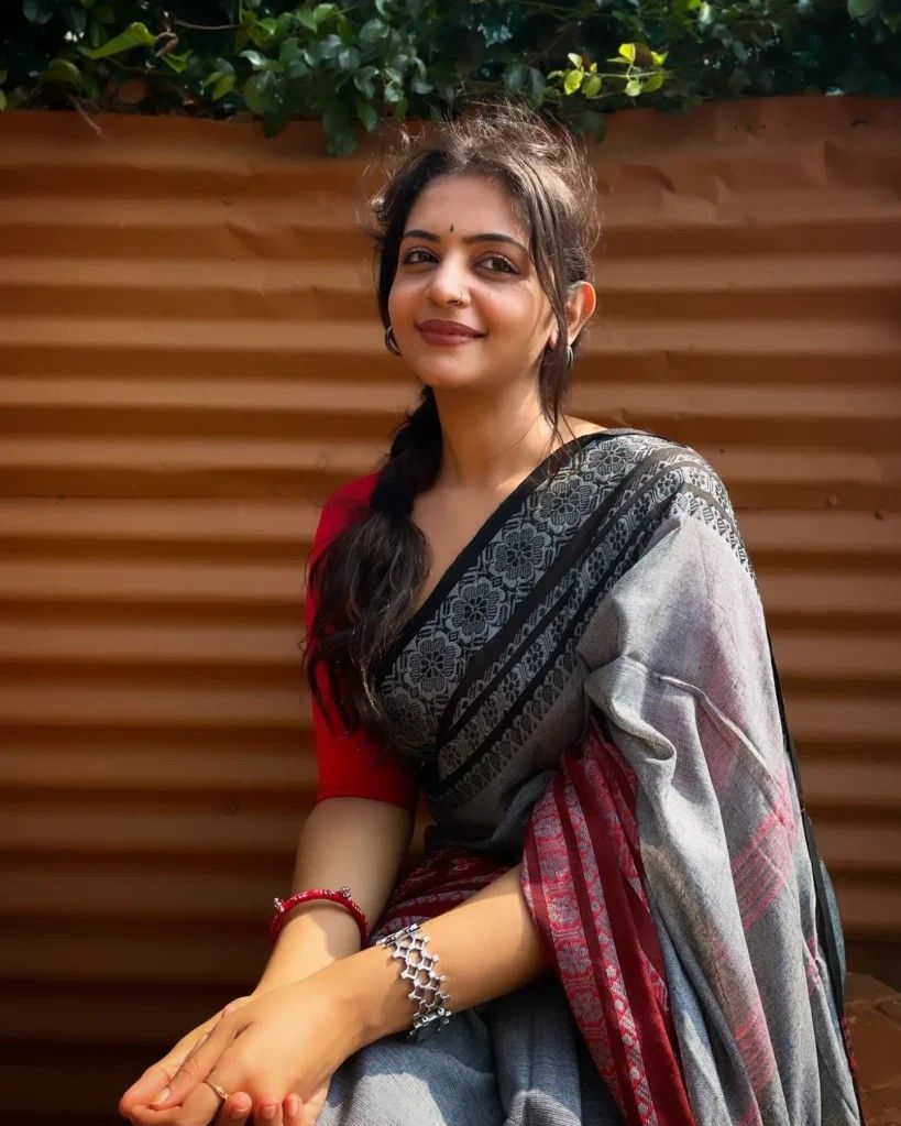 Aiswarya Mithun Koroth seated in a grey and red saree outdoors