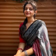 Aiswarya Mithun Koroth seated in a grey and red saree outdoors