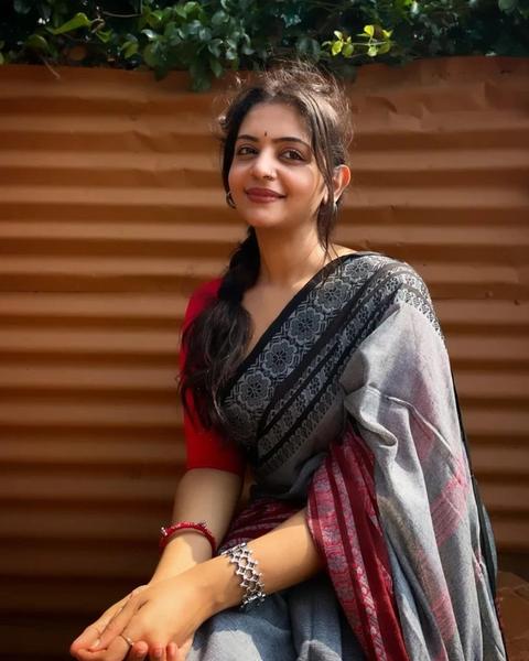 Aiswarya Mithun Koroth seated in a grey and red saree outdoors