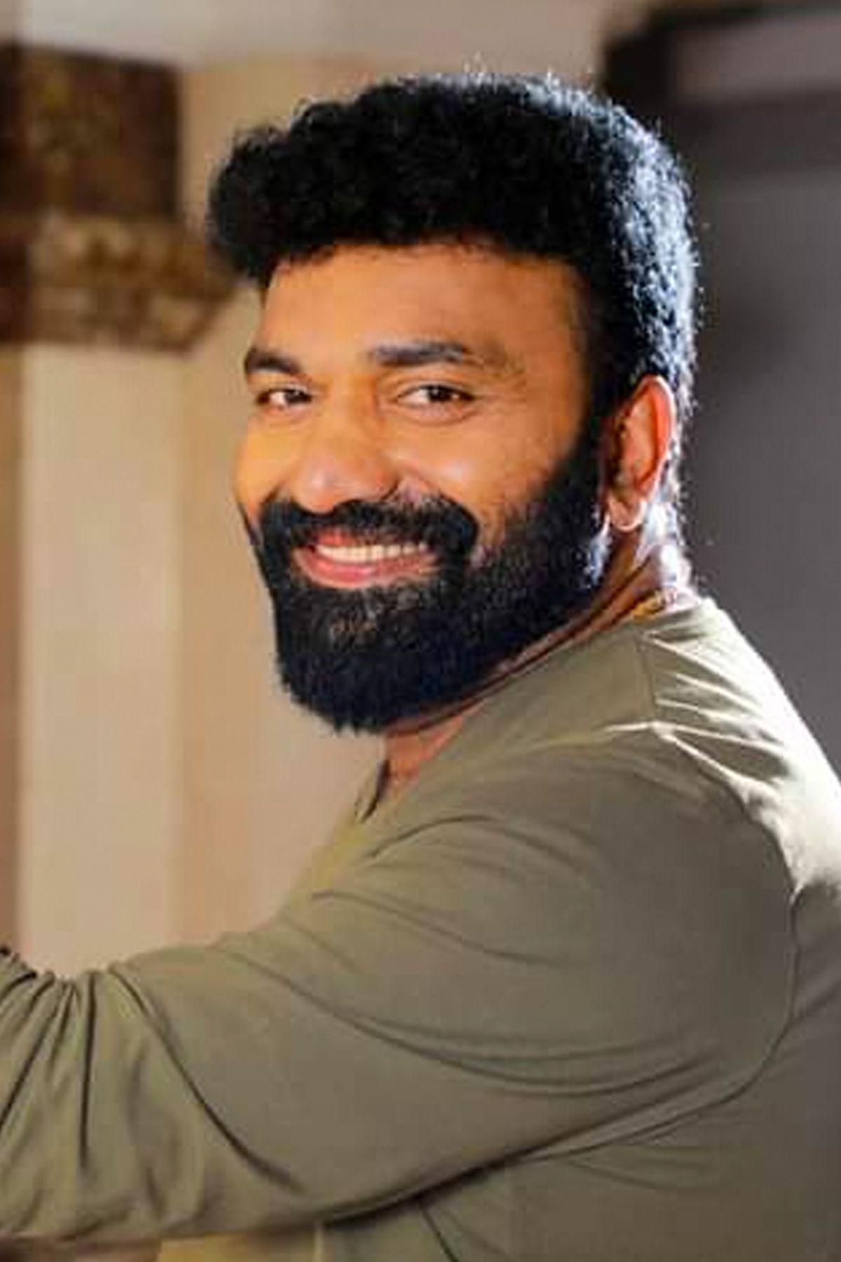 Kottayam Nazeer with a beard in an olive shirt, smiling portrait