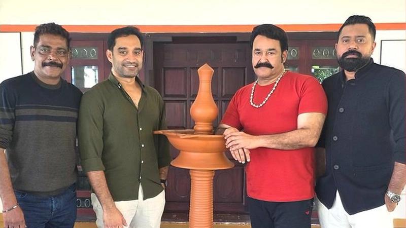 Mohanlal in a red shirt beside a traditional lamp with two men