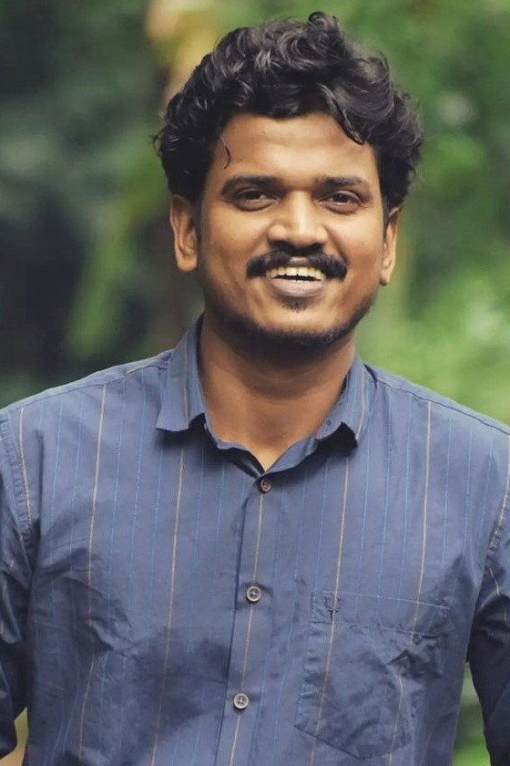 Lukman Avaran smiling in a blue striped shirt against green foliage, portrait