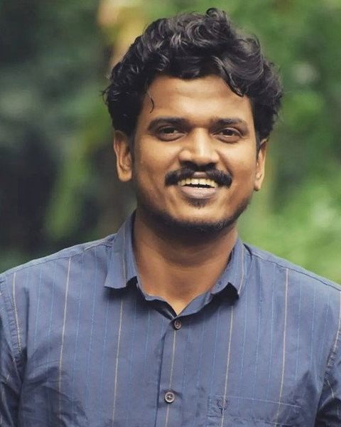 Lukman Avaran smiling in a blue striped shirt against green foliage, portrait