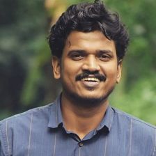 Lukman Avaran smiling in a blue striped shirt against green foliage, portrait