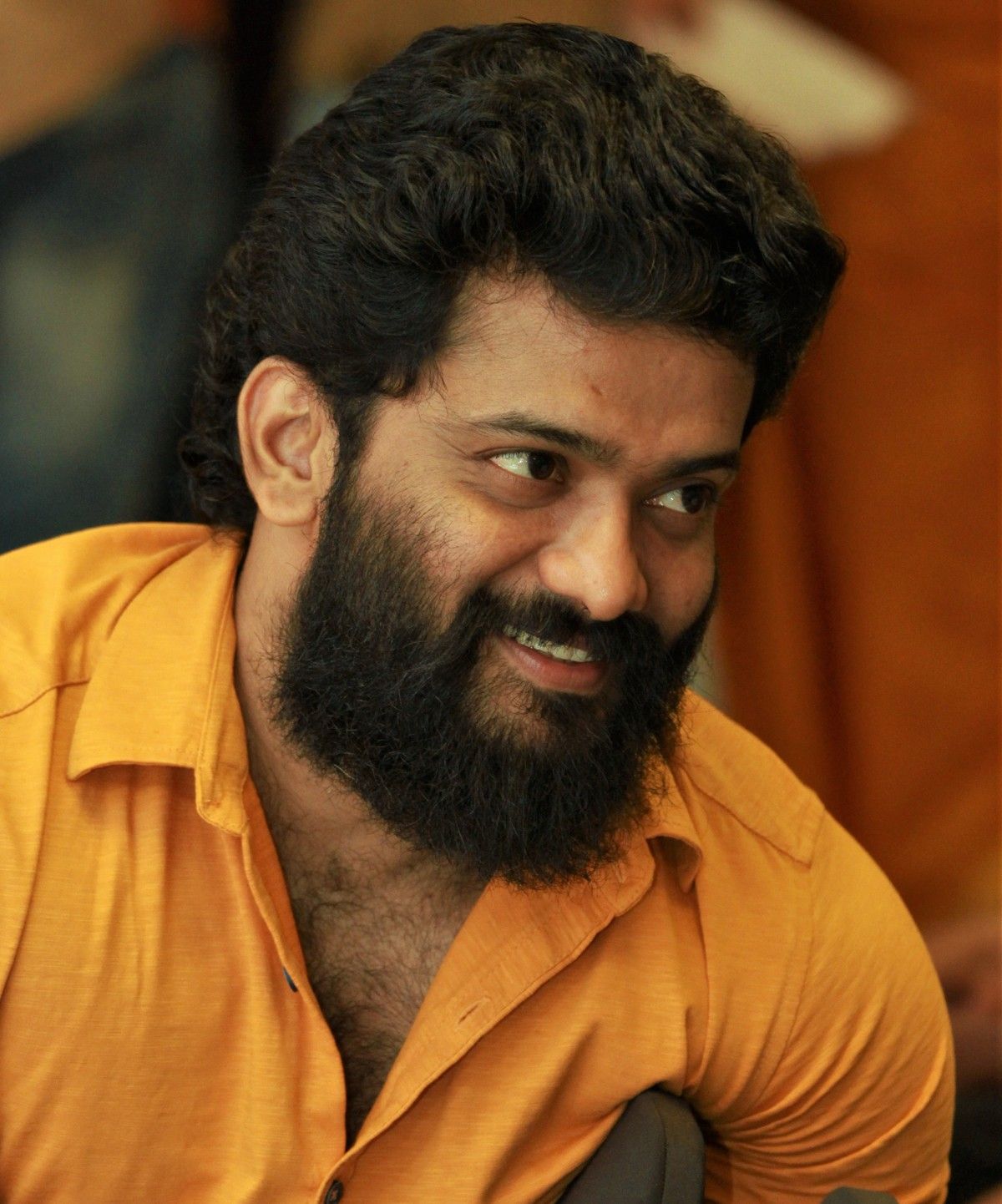Manikuttan smiling with a full beard and thick wavy hair, in a mustard yellow shirt, candid portrait