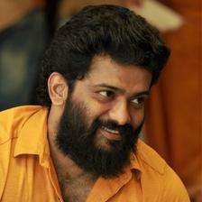 Manikuttan smiling with a full beard and thick wavy hair, in a mustard yellow shirt, candid portrait