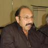 Sathyaraj in glasses speaking at a press event table