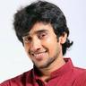 Dhruvan smiling in a maroon shirt against a white background