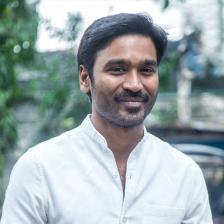 Dhanush smiling in a white shirt outdoors, half-length portrait