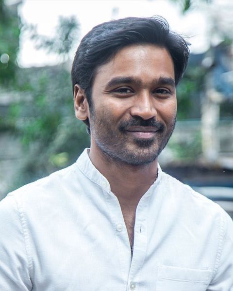 Dhanush smiling in a white shirt outdoors, half-length portrait